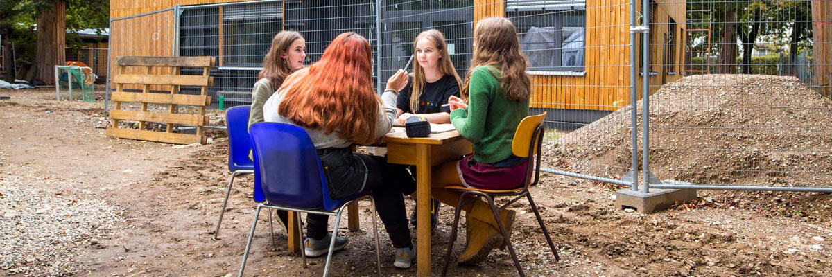 4 Schülerinnen an einem Tisch vor einer Baustelle