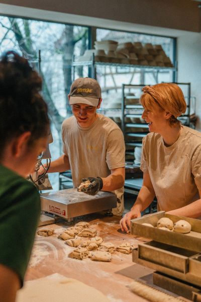brotique Eine männlich gelesene und zwei weiblich gelesene Personen bereiten Brotwaren zu.