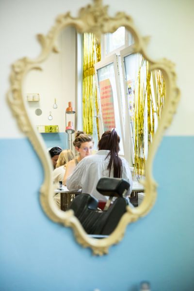Zwei weiblich gelesene Personen spiegeln sich in einem verzierten Spiegel.