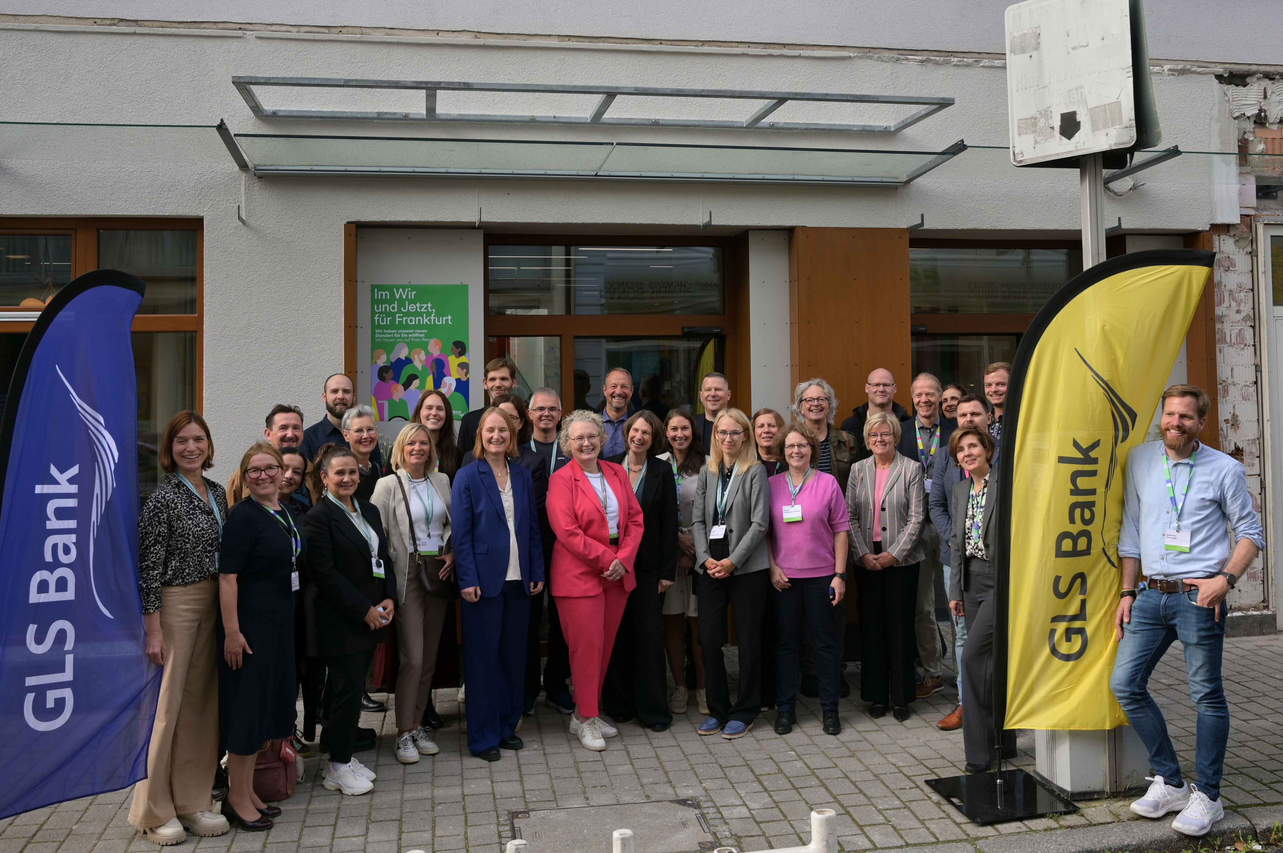 GLS Bank Frankfurt: Eine Gruppe von Menschen posiert gemeinsam vor einem Gebäude mit GLS Bank-Bannern.
