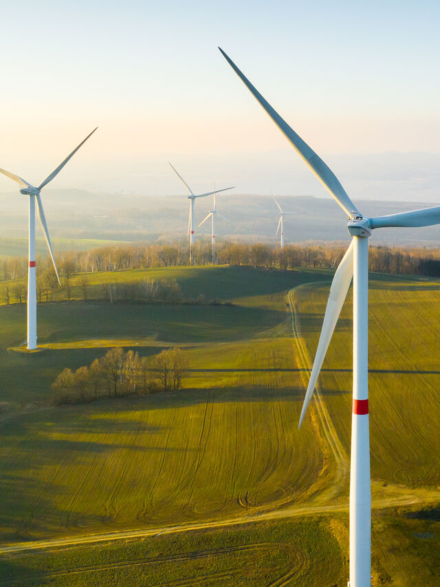 Windkraftanlagen stehen auf grasbewachsenen Hügeln unter einem klaren Himmel in einer ländlichen Landschaft.