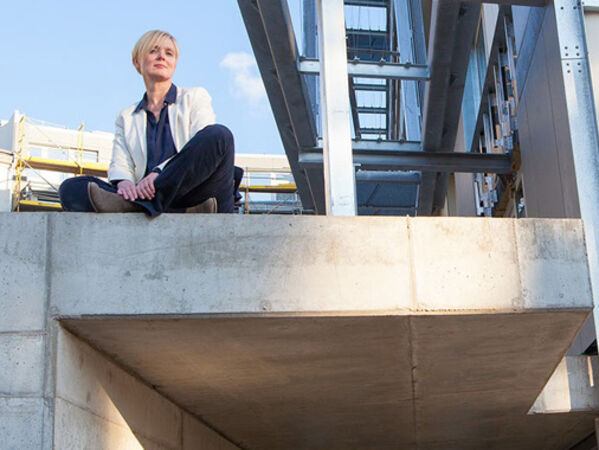 Weiblich gelesene Person sitzt im Schneidersitz auf einer Betonwand.