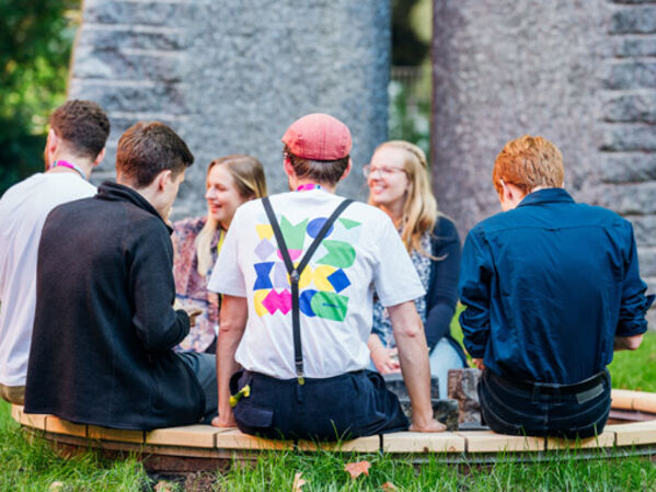 Menschen sitzen auf einer Holzbank im Kreis und unterhalten sich