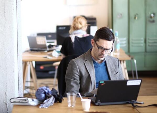 Männlich gelesene Person am Schreibtisch mit Laptop.