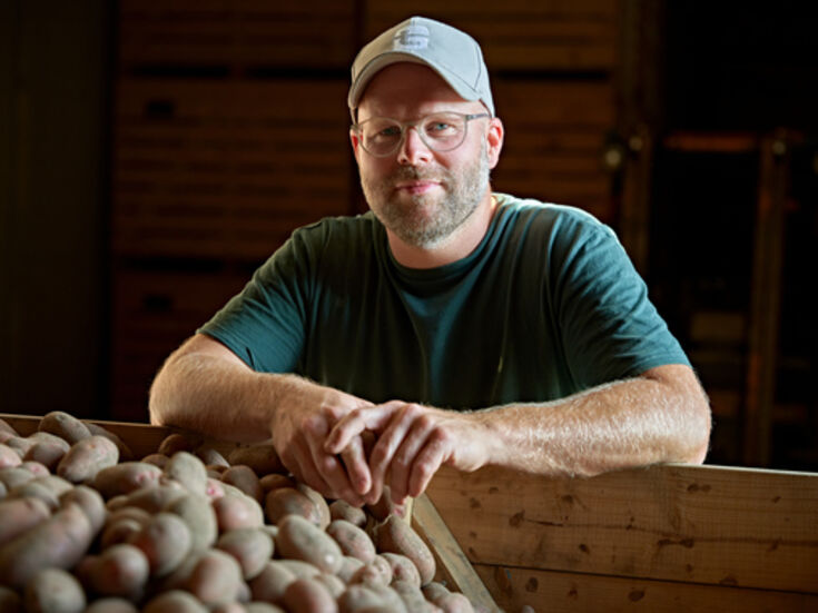 Mann mit  Brille und Schiebermütze an einer Kiste, die mit Kartoffeln gefüllt ist.
