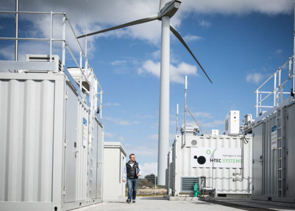 Männlich gelesene Person vor einem Windrad.