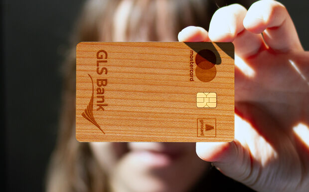 Weiblich gelesene Person hält Holzkarte der GLS Bank vor das Gesicht