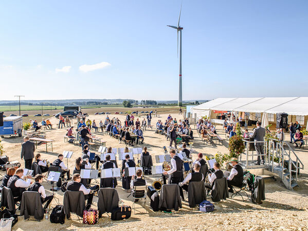 Eine Band spielt unter freiem Himmel in der Nähe eines Zelts, in dem Menschen sitzen und ein Windrad steht.
