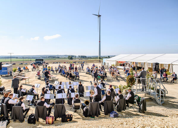 Eine Band spielt unter freiem Himmel in der Nähe eines Zelts, in dem Menschen sitzen und ein Windrad steht.