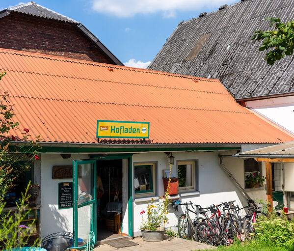 Kleiner Hofladen mit rotem Dach, Fahrrädern vor der Tür und einem gelben Schild.