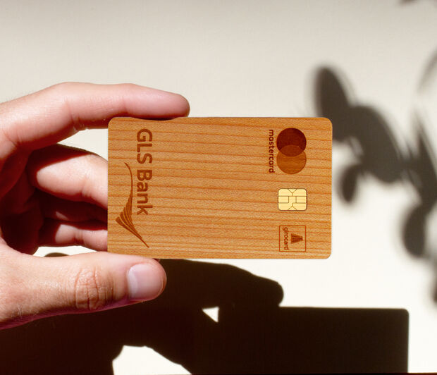 Holzkarte der GLS Bank vor weißer Wand, auf der Schatten einer Pflanze zu sehen sind