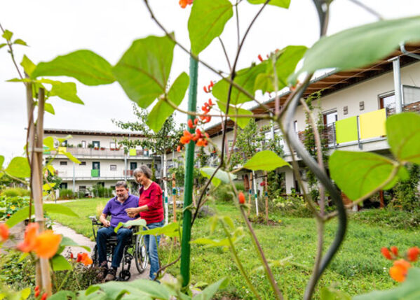 Weiblich gelesene und männlich gelesene Person im Rollstuhl in einen Garten.
