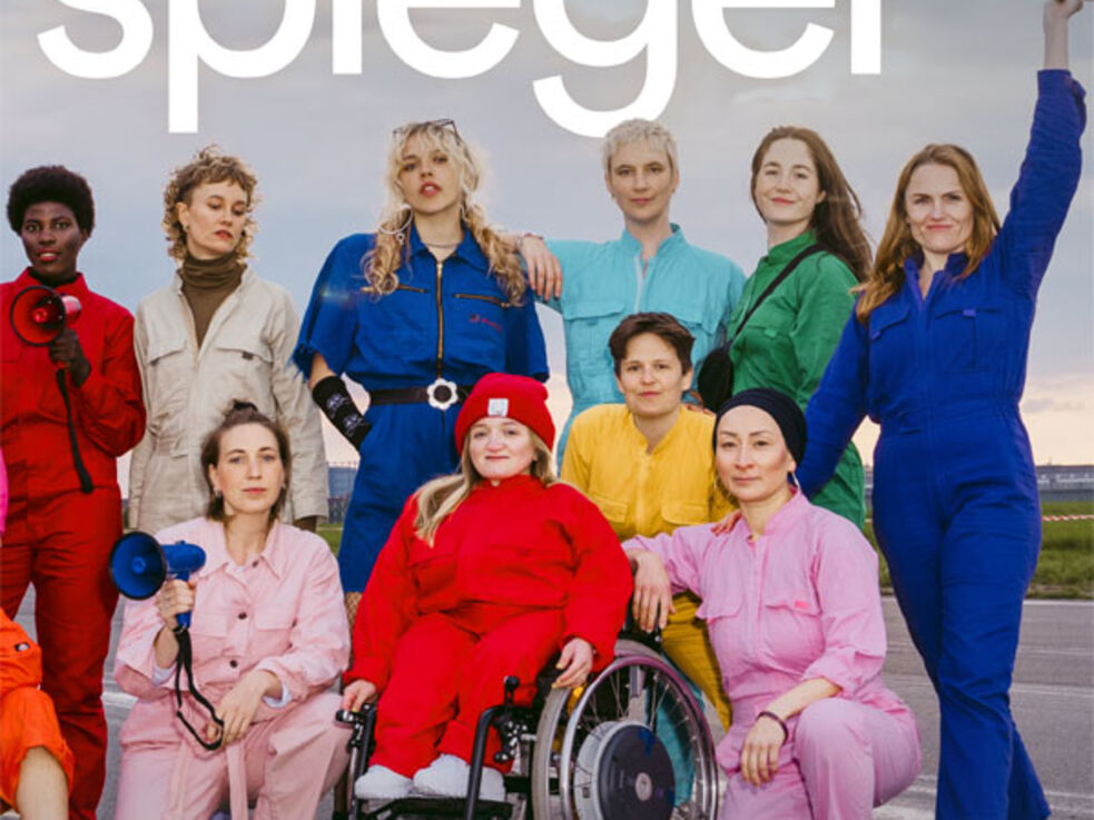 Zwölf Menschen in bunten Overalls posieren an einem bewölkten Tag selbstbewusst im Freien.