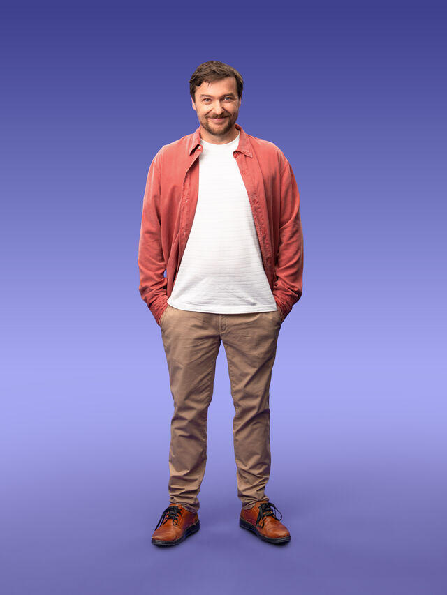 Sebastian Sladek mit offenem rotem Hemd und weißem T-shirt vor lila Hintergrund