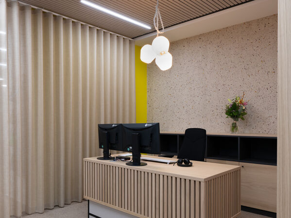 Moderner Empfangstresen mit zwei Monitoren, einem Stuhl und einer Vase mit Blumen.