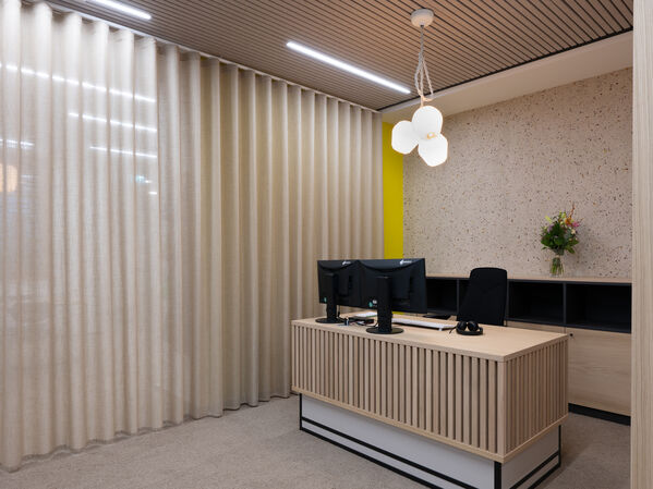 Moderner Empfangstresen mit zwei Monitoren, einem Stuhl und einer Vase mit Blumen.