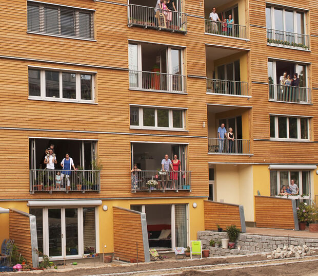 Tagsüber stehen Menschen auf den Balkonen eines modernen Wohnhauses aus Holz.