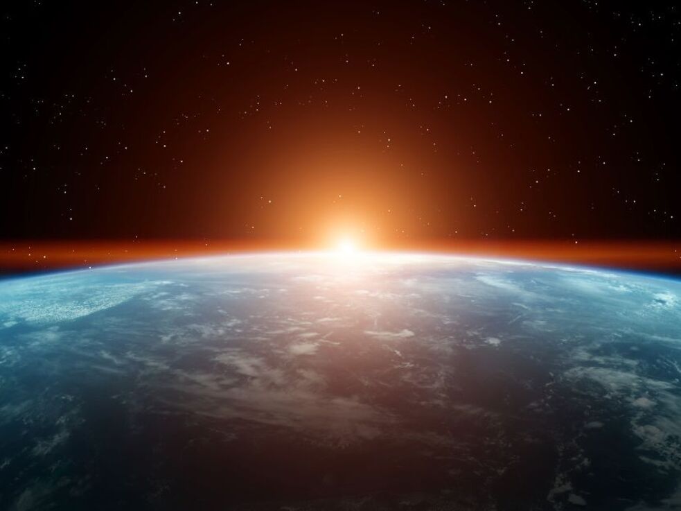 Die Sonne geht über der Erde auf, aus der Perspektive des Weltraums betrachtet, vor einem Hintergrund voller Sterne.