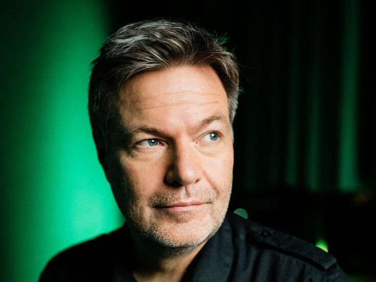 Ein Mann mittleren Alters in einem schwarzen Hemd blickt bei grünem Licht zur Seite.