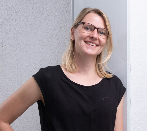 Eine Frau in schwarzer Kleidung und mit Brille, die lächelt und mit einer Hand in der Hüfte steht.