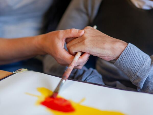 GLS Kunde Raphaelhaus Stuttgart Eine Hand hilft einer anderen beim Malen mit einem Pinsel.