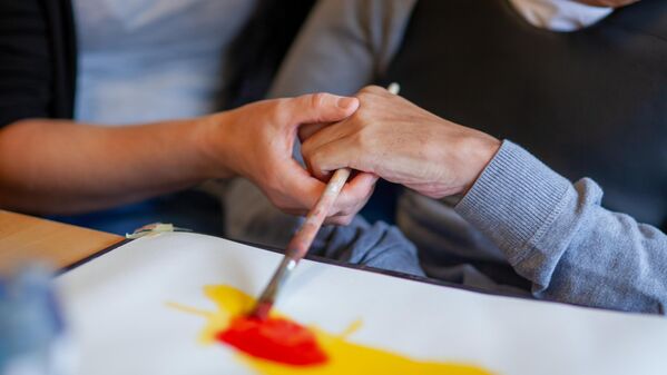 Eine Hand hilft einer anderen beim Malen mit einem Pinsel.