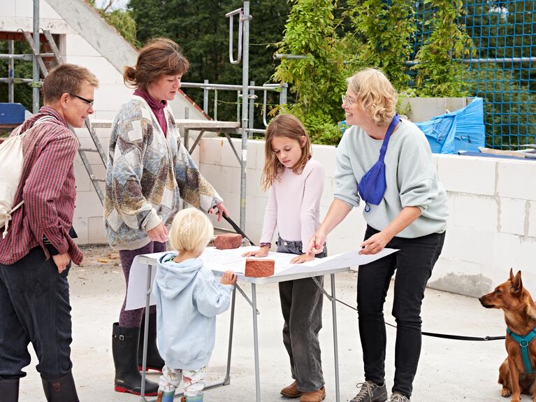 Mehrere weiblich gelesene Personen, ein Kind und ein Hund stehen in einem Rohbau.