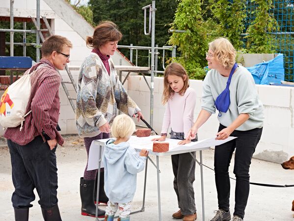 Mehrere Menschen stehen in einem Rohbau an einem Tisch und studieren Baupläne