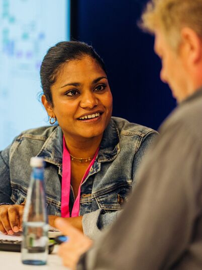 Junge weiblich gelesene Person of Color spricht mit einer männlich gelesenen Person.