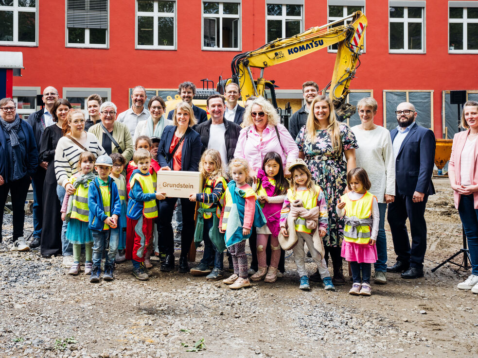 Erwachsene und Kinder vor einem Bagger auf einer Baustelle