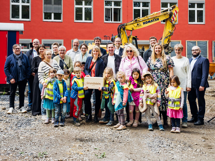 Erwachsene und Kinder vor einem Bagger auf einer Baustelle
