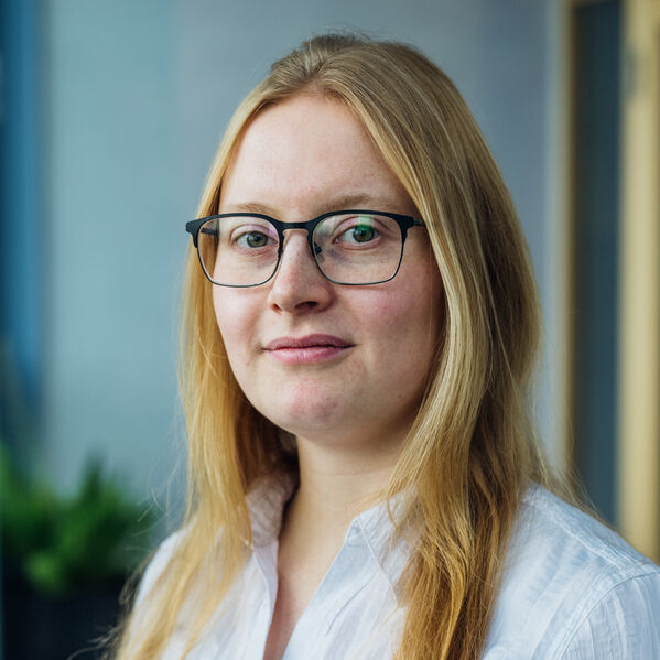Eine junge weiblich gelesene Person mit blonden langen Haaren und Brille.