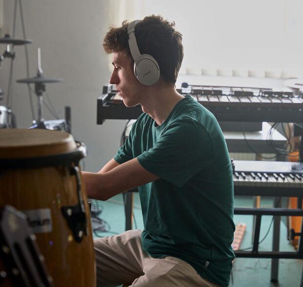Junge Person mit Kopfhörern, die in einem Musikstudio an einem Keyboard sitzt.