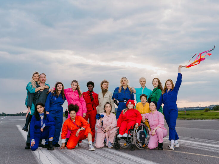 Eine bunte Gruppe von Menschen in farbenfrohen Jumpsuits posiert gemeinsam auf einem Laufsteg.