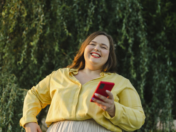 Weiblich gelesene Person lachend mit Smartphone on der Hand.