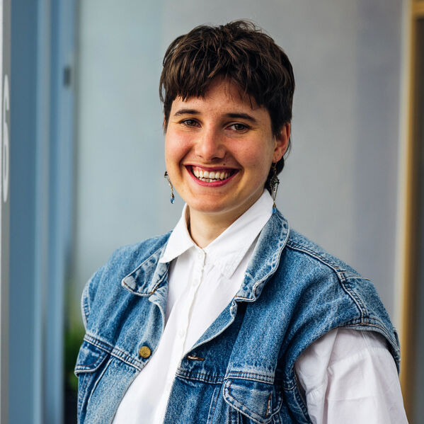Eine junge lächelnde Person mit braunen kurzen Haaren.