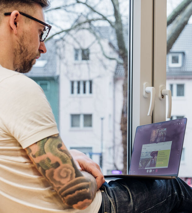 Mann sitzt mit Laptop auf einer Fensterbank in einer Videoberatung.