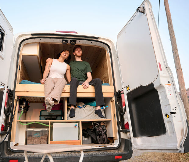 Weiblich und männlich gelesene Person sitzen im ausgebauten Camper in der Natur