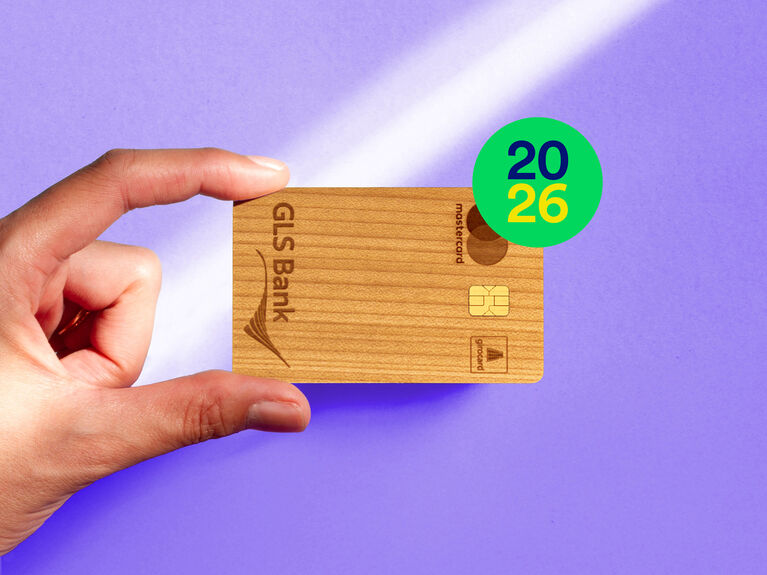 Eine Hand hält eine GLS Bank Mastercard vor einem violetten Hintergrund mit der Jahreszahl 2026 in einem Kreis.