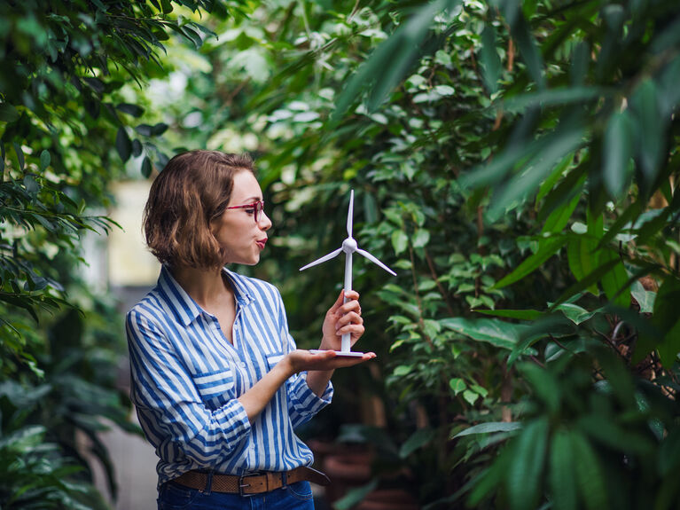 Eine Frau hält ein kleines Windradmodell inmitten von Grünpflanzen.