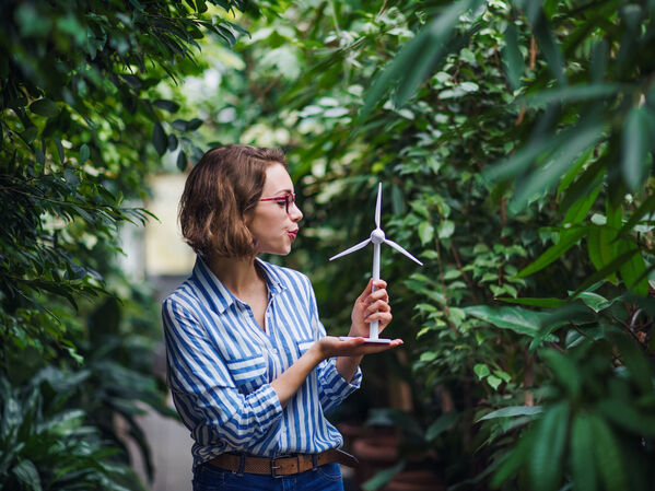Eine Frau hält ein kleines Windradmodell inmitten von Grünpflanzen.
