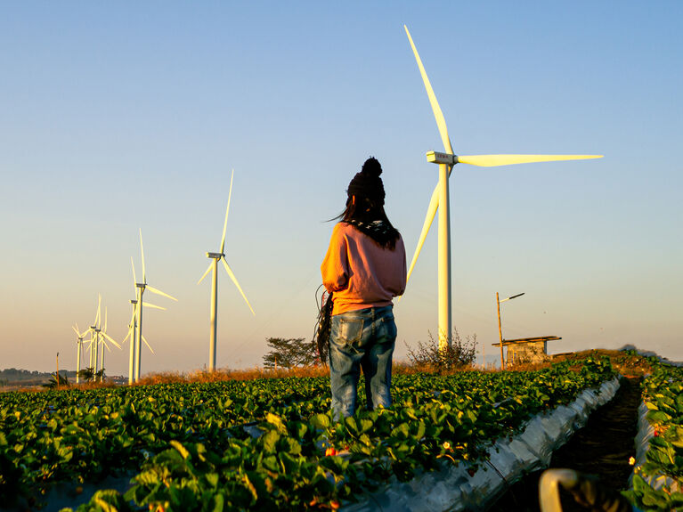 Eine Person steht auf einem Feld mit Windkraftanalagen.