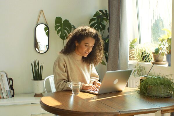 Frau mit Laptop an einem Holztisch. Im Hintergrund grüne Pflanzen.
