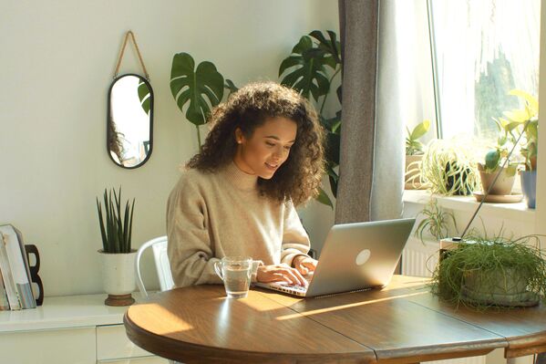 Frau mit Laptop an einem Holztisch. Im Hintergrund grüne Pflanzen.