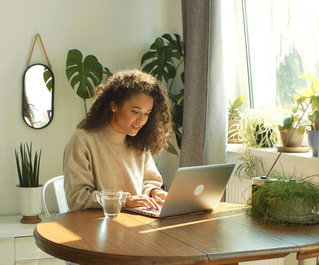 Frau am Tisch mit Laptop und Tee, Pflanzen im Hintergrund