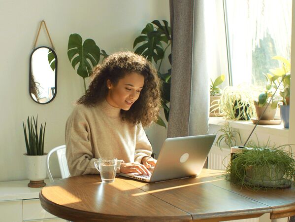 Frau mit Laptop an einem Holztisch. Im Hintergrund grüne Pflanzen.