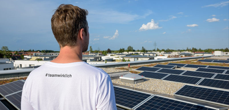 Jetzt individuelles Solarkonzept erstellen mit dem GLS Solar-Rechner - Mann sieht über Photovoltaik-Anlagen auf Dächern