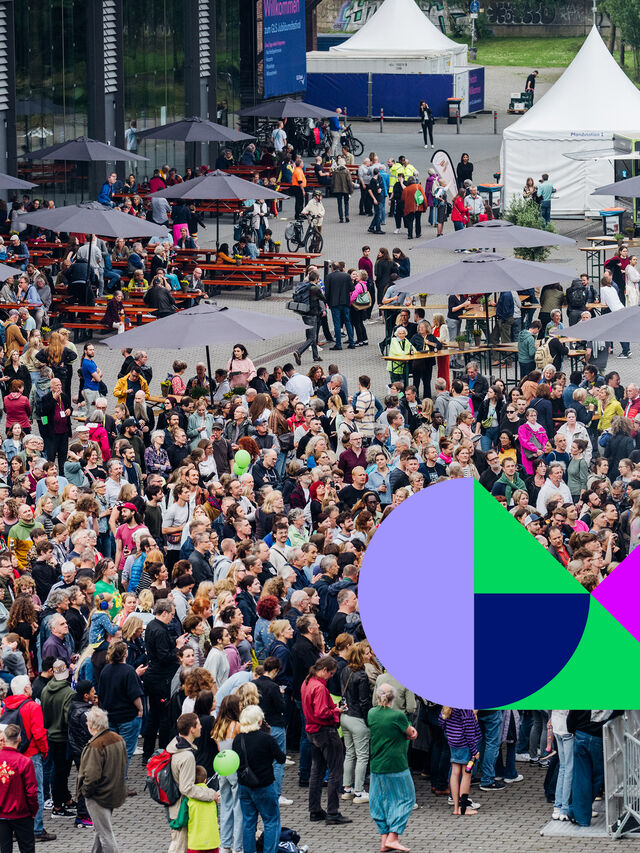 Große Menschenmenge bei einem Festival im Freien mit Zelten und der Aufschrift Gutes Morgen Festival.
