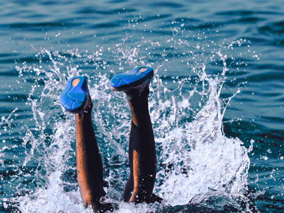 Beine einer Person, die mit Schwimmschuhen ins Wasser eintaucht