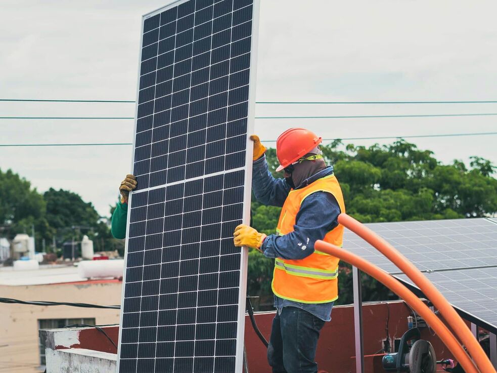 Ein Arbeiter in Schutzkleidung installiert ein Solarmodul auf einem Dach.